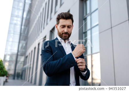 Smiling confident calm attractive young caucasian male ceo manager with beard in suit near modern office building 94351027