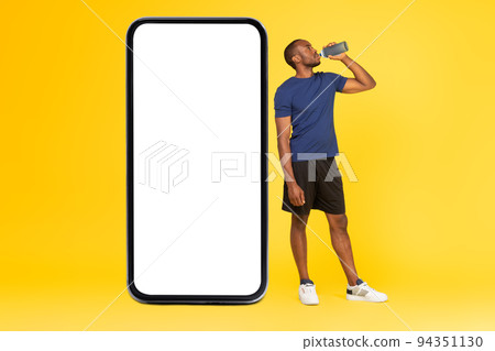 African Guy Near Cellphone Big Screen Drinking Water, Yellow Background 94351130