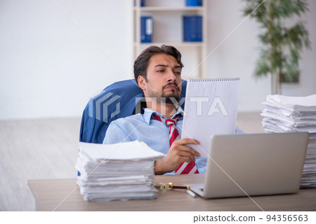 Young male employee and too much work in the office Young male employee and too much work in the office 94356563