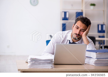 Young male employee unhappy with excessive work in the office Young male employee unhappy with excessive work in the office 94356985