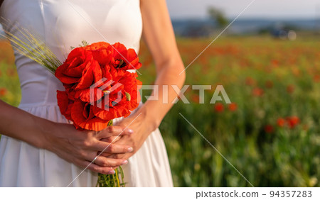 Bride in a white dress holding a bouquet of poppy flowers, warm sunset time on the background of the red poppy field. Copy space. The concept of calmness, silence and unity with nature. Bride in a white dress holding a bouquet of poppy flowers, warm sunset time on the background of the red poppy field. Copy space. The concept of calmness, silence and unity with nature. 94357283
