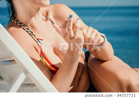 Woman in rainbow bikini. Happy tanned well looking middle aged woman in rainbow swimsuit at seaside, blue sea water in background. Holiday, vacation and recreational concept. 94357711