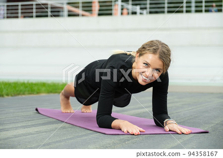 Fit happy woman working on abdominal muscles doing plank exercise on a purple fitness rug outside 94358167