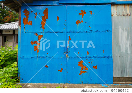 A warehouse with a blue door where the paint has peeled off 94360432