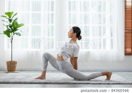 Happy Athletic Asian woman practice yoga stretching pose for stretching muscle for warm up with meditation smile,Healthy female doing yoga exercise and relax at home. Yoga self care Healthcare Concept 94360566