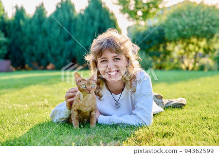 Outdoor portrait of teenage girl with pet cat in arms lying on grass Outdoor portrait of teenage girl with pet cat in arms lying on grass 94362599