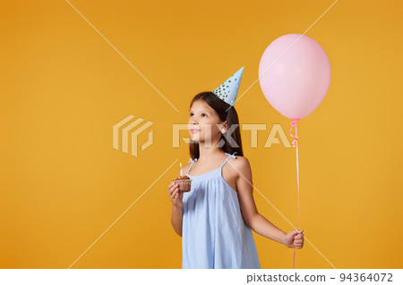 happy little birthday girl with party cone holding cupcake 94364072