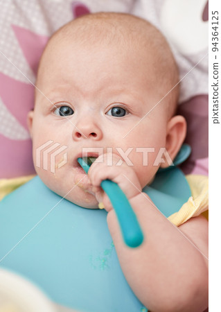 cute baby girl eating with spoon in kitchen 94364125