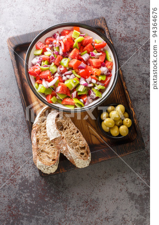 Salad of bell green peppers, tomatoes and onions served with olives and homemade bread close-up on a wooden board. Vertical top view 94364676