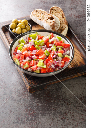Salad of bell green peppers, tomatoes and onions served with olives and homemade bread close-up on a wooden board. Vertical 94364681