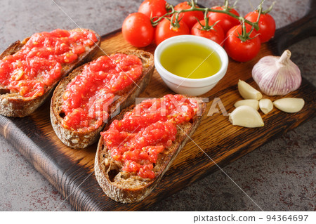 Catalan Pan con Tomate Spanish toasted bread rubbed with fresh garlic and ripe tomato, then drizzled with olive oil closeup on the wooden board. Horizontal Catalan Pan con Tomate Spanish toasted bread rubbed with fresh garlic and ripe tomato, then drizzled with olive oil closeup on the wooden board. Horizontal 94364697