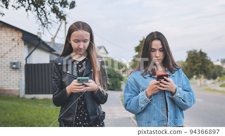 Two girlfriends watch a smartphone and walk through the village. 94366897