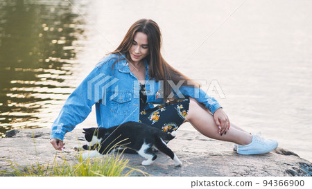 A girl plays with a cat by the lake. 94366900