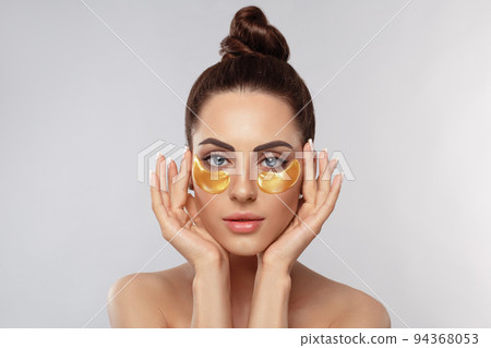 Beauty model girl face with healthy fresh skin. Woman with under eye collagen gold pads.  Skin care concept, anti-aging moisturizing eye mask, golden hydrogel patches, eye skin treatment, cosmetology 94368053