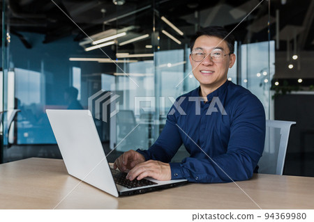 Young and successful asian businessman in glasses working on laptop inside modern office building, happy manager smiling and looking at camera, entrepreneur investor portrait. Young and successful asian businessman in glasses working on laptop inside modern office building, happy manager smiling and looking at camera, entrepreneur investor portrait. 94369980