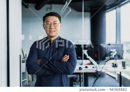 Portrait of successful Asian programmer, team leader company owner smiling and looking at camera with crossed arms, talented startup entrepreneur working inside IT office Portrait of successful Asian programmer, team leader company owner smiling and looking at camera with crossed arms, talented startup entrepreneur working inside IT office 94369982