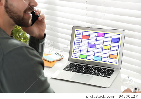 Young man using calendar app on laptop in office, closeup 94370127