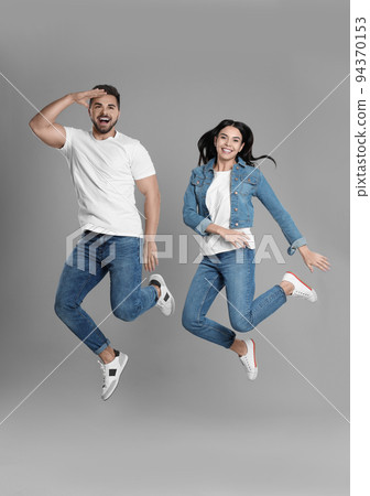 Young couple in stylish jeans jumping on grey background Young couple in stylish jeans jumping on grey background 94370153
