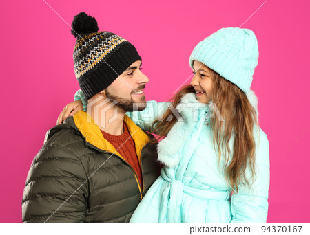 Happy father and daughter in warm clothes on pink background. Winter vacation 94370167