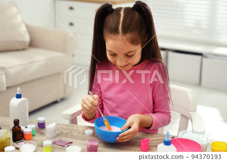 Cute little girl mixing ingredients with silicone spatula at table. DIY slime toy Cute little girl mixing ingredients with silicone spatula at table. DIY slime toy 94370193