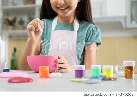 Little girl mixing ingredients with silicone spatula at table in kitchen, closeup. DIY slime toy 94370202
