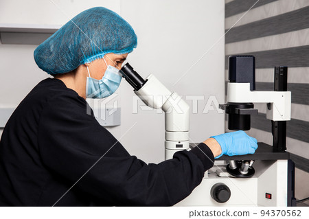 Female scientist looking at slides with patient samples using an inverted microscope in the laboratory. Female scientist looking at slides with patient samples using an inverted microscope in the laboratory. 94370562