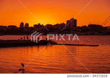 People on pier with sunset sky and reflection on water in Florianopolis 94371029
