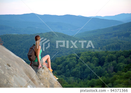 Tired hiker girl relaxing on rocky mountain top enjoying evening nature during travelling on wilderness trail. Lonely woman traveler traversing high hilltop route. Healthy lifestyle concept Tired hiker girl relaxing on rocky mountain top enjoying evening nature during travelling on wilderness trail. Lonely woman traveler traversing high hilltop route. Healthy lifestyle concept 94371366