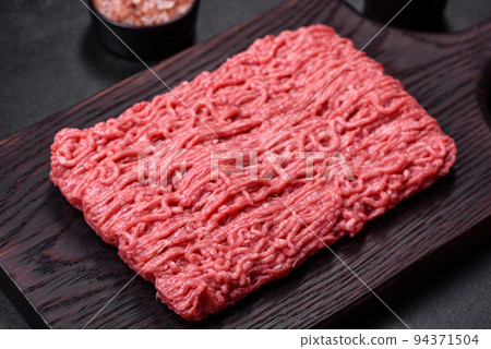Fresh minced beef on cutting board on dark background with ingredients for cooking Fresh minced beef on cutting board on dark background with ingredients for cooking 94371504