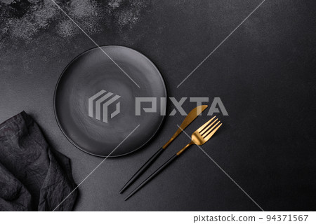 An empty black plate on a dark concrete background with spices, herbs and cutlery An empty black plate on a dark concrete background with spices, herbs and cutlery 94371567