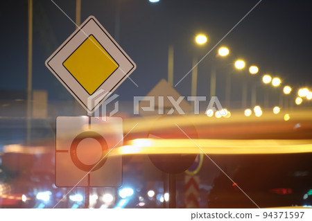 Roundabout road signs with blurred cars on city street traffic at night. Urban transportation concept Roundabout road signs with blurred cars on city street traffic at night. Urban transportation concept 94371597