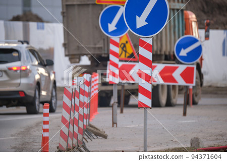 Roadworks warning traffic signs of construction work on city street and slowly moving cars Roadworks warning traffic signs of construction work on city street and slowly moving cars 94371604