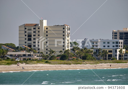 Resort beach with white sand, blue water, tall hotel buildings. Happy people sunbathing and swimming in ocean Resort beach with white sand, blue water, tall hotel buildings. Happy people sunbathing and swimming in ocean 94371608