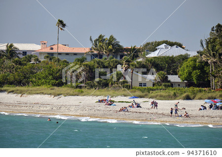 Resort beach with white sand, blue ocean water, row of comfortable hotel cottages houses under blue tropical sun 94371610