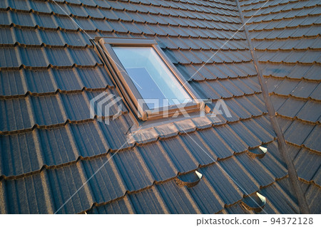 Closeup of attic window on house roof top covered with ceramic shingles. Tiled covering of building 94372128