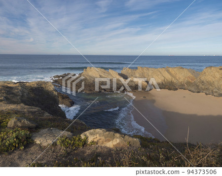 View of empty Praia dos Buizinhos sand beach with ocean waves and sharp rock and cllifs at wild Vicentina coast in Porto Covo, Portugal. Golden hour. View of empty Praia dos Buizinhos sand beach with ocean waves and sharp rock and cllifs at wild Vicentina coast in Porto Covo, Portugal. Golden hour. 94373506