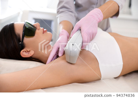 Young woman undergoing laser epilation procedure in beauty salon 94374836