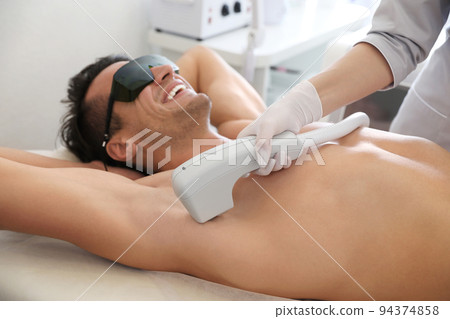 Young man undergoing laser epilation procedure in beauty salon 94374858