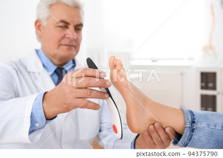 Male orthopedist fitting insole on patient's foot in clinic 94375790