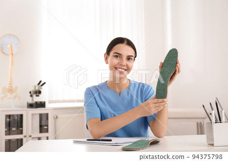 Young female orthopedist showing insole in clinic Young female orthopedist showing insole in clinic 94375798