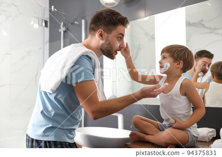 Dad and son with shaving foam on their faces having fun in bathroom 94375831