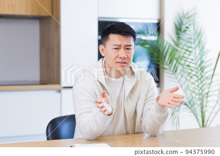Asian man talking online on video call at home in living room or kitchen. male in casual clothes looking at camera, meeting or conference in distance. Portrait teacher. Lecture training. Webcam view Asian man talking online on video call at home in living room or kitchen. male in casual clothes looking at camera, meeting or conference in distance. Portrait teacher. Lecture training. Webcam view 94375990