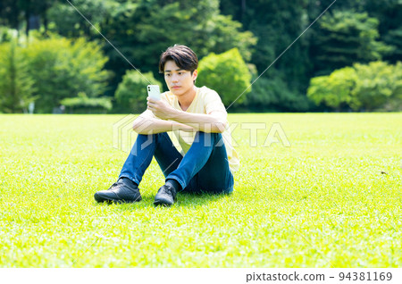年輕人坐在草地上，看著智能手機 94381169