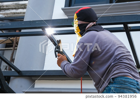 The welder is welding the steel structure to add to the house The welder is welding the steel structure to add to the house 94381956