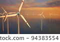 Large wind turbines with blades in field aerial view bright orange sunset blue sky wind park slow motion drone turn. Silhouettes windmills, large orange sun disc summer lens flare. Alternative energy 94383554