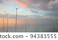 Large wind turbines with blades in field aerial view bright orange sunset blue sky wind park slow motion drone turn. Silhouettes windmills, large orange sun disc summer lens flare. Alternative energy 94383555