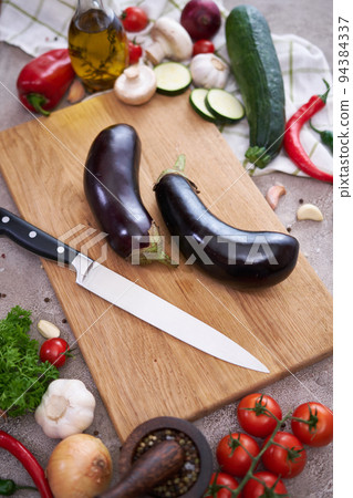 eggplant on wooden cutting board and vegetables at domestic kitchen eggplant on wooden cutting board and vegetables at domestic kitchen 94384337