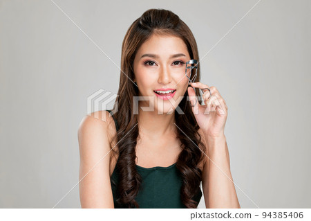 Young ardent female model with flawless beautiful skin using eyelash curler. 94385406