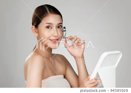 Young ardent woman model with flawless beautiful skin using eyelash curler. 94385929