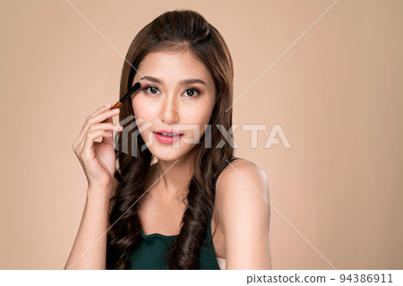Portrait of ardent female model applying her eyeshadow and holding a mirror. Portrait of ardent female model applying her eyeshadow and holding a mirror. 94386911
